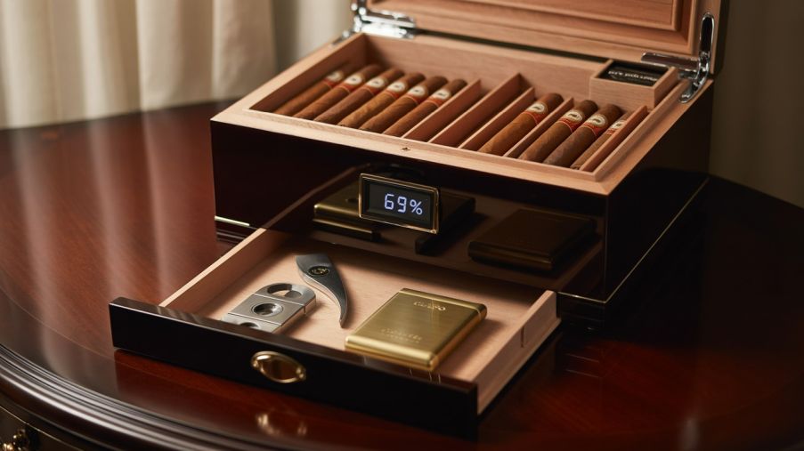Luxury wooden humidor with cigars, digital hygrometer reading 69%, and drawer containing cigar cutter and accessories.